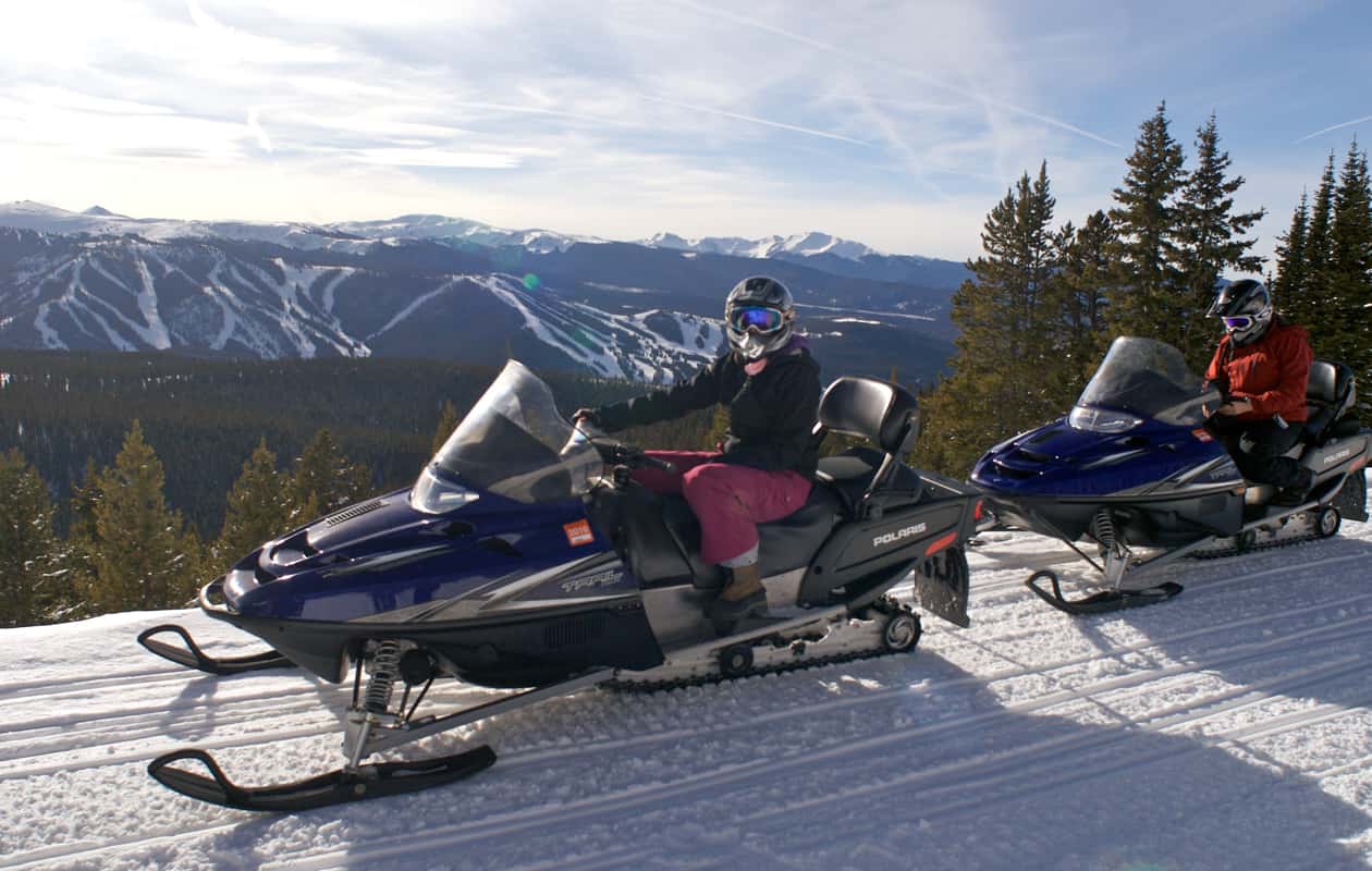 Two people on snow mobiles in front of a Colorado backdrop