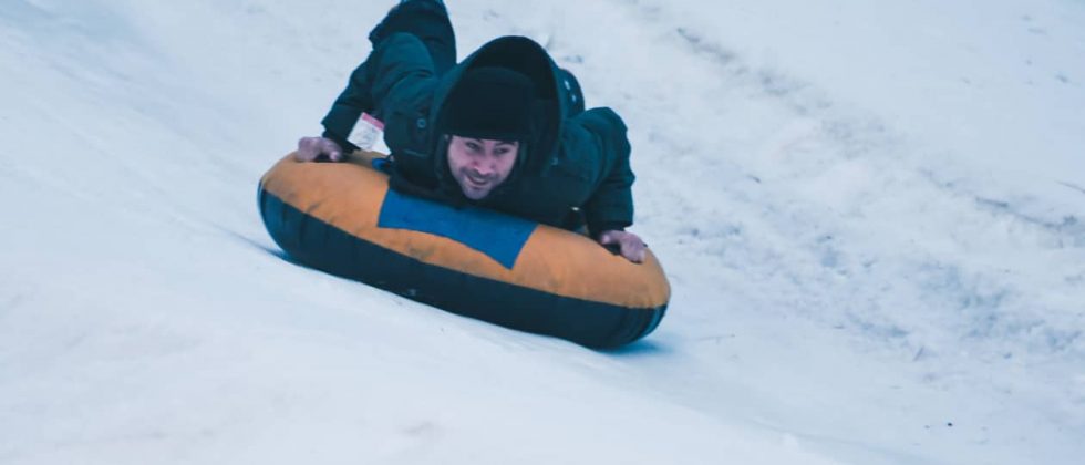 Man riding a snow tub down a hill